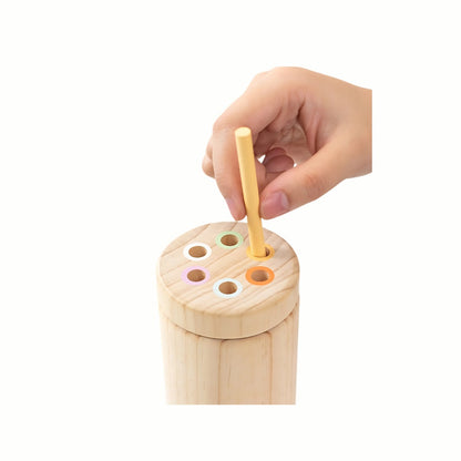A  hand inserting a stick into the correct colored slot of the container from the Wooden Balance and Posting Sticks Game, developing color matching and fine motor skills.