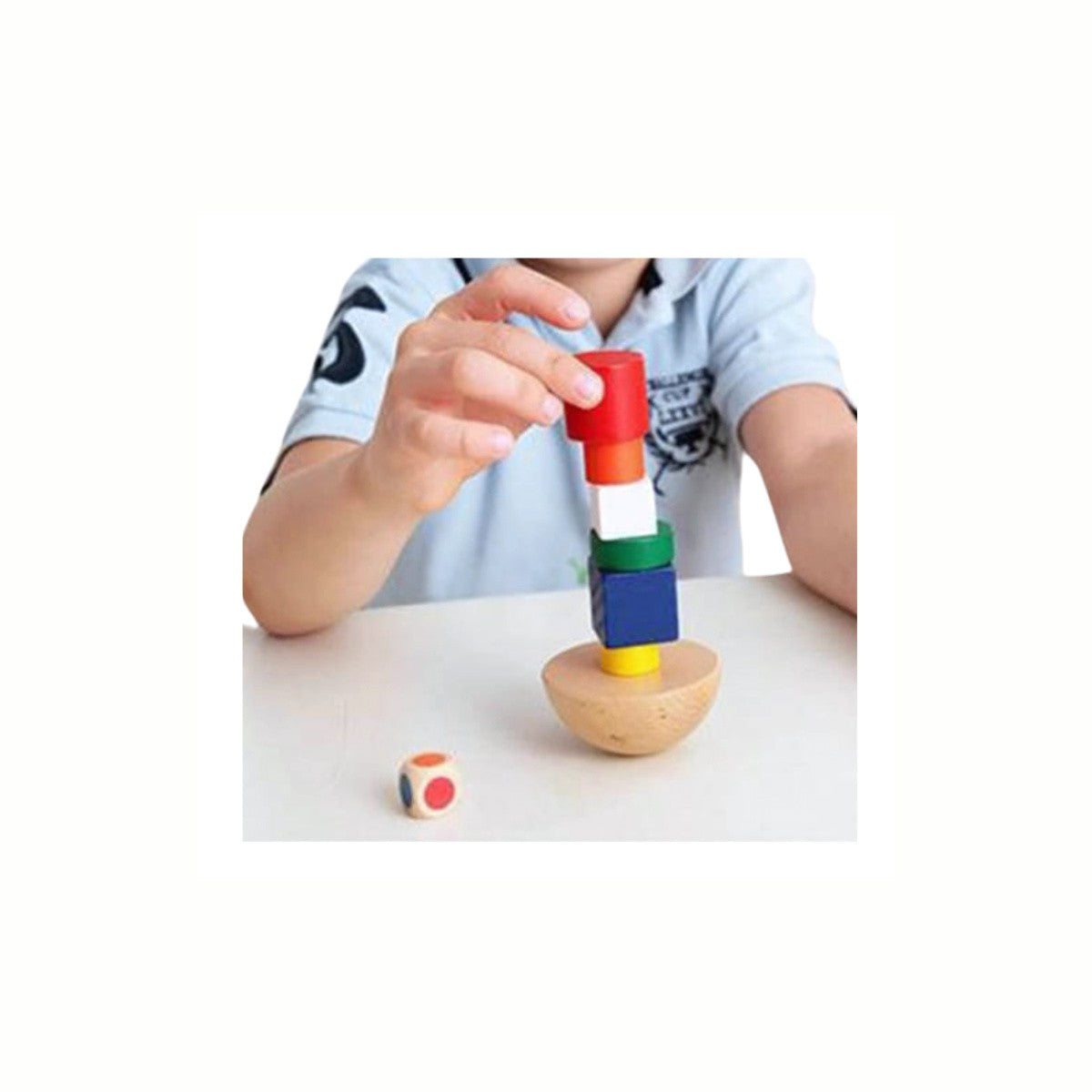 A child's hand carefully stacking a block onto the Wooden Balance Blocks Game tower, demonstrating the effort required for balance and precision.