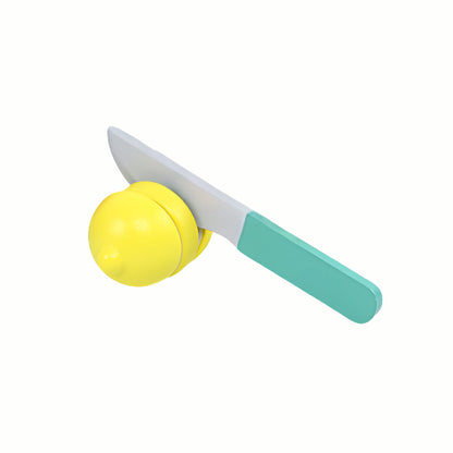 A  hand cutting the wooden fruit with the toy knife from the Wooden Blender and Fruit Set, demonstrating fine motor skills and the realistic cutting action.